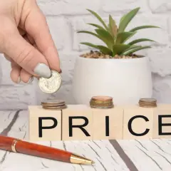 Dłoń kładzie monetę na kostce z literą "P", obok kostek z napisem "RICE". Zastanawiasz się, o ile służebność obniża wartość nieruchomości?