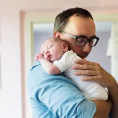 Ojciec tuli śpiące dziecko, delikatnie je kołysząc. Oklepywanie dziecka to moment bliskości i troski.