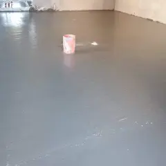 Świeżo wylany, gładki **pianobeton** na podłodze. W tle widać wiaderko i instalacje.