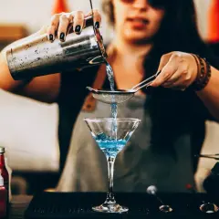 Barman przelewa niebieski płyn z shakera przez sitko do kieliszka. Może to być przyszłość, gdzie wódka w proszku stanie się rzeczywistością.