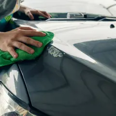 Manos puliendo el capó de un coche gris con un paño verde, mostrando cómo quitar arañazos del coche.