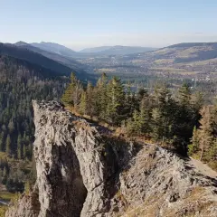 Widok z Nosala, góry samobójców, na Tatry i Zakopane. Skalisty szczyt, las i dolina.