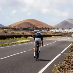 Ciclista pedaleando por una carretera en Lanzarote, rodeado de paisajes volcánicos y casas blancas. Una experiencia única de lanzarote en bici.