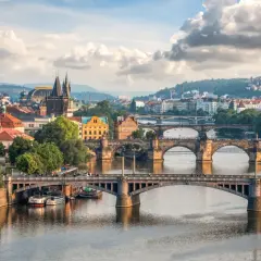 Widok na wiele mostów w Czechach, w tym Most Karola, nad Wełtawą, z praskim zamkiem i wzgórzami w tle.