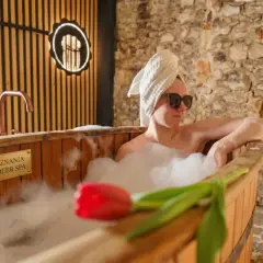 Relaks w beer spa w Zakopanem. Kobieta w wannie z pianą, ręcznikiem na głowie i okularach przeciwsłonecznych, obok piwo i tulipan.