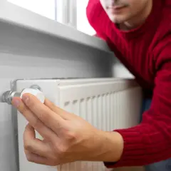 Mężczyzna w czerwonym swetrze reguluje zawór grzejnika, pokazując, jak odpowietrzyć grzejnik.