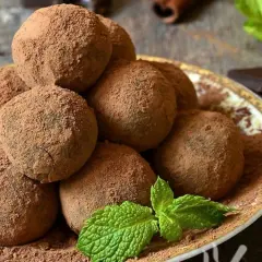 Un mucchio di tartufi al cioccolato facili e veloci, spolverati di cacao, su un piatto decorato, con menta fresca e un pezzetto di cioccolato fondente.