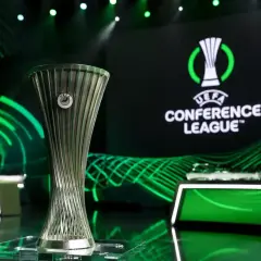 Trofeum Ligi Konferencji UEFA na tle logo i zielonych świateł. Marzenie o wygraniu tych rozgrywek napędza emocje podczas meczów ligi konferencji.