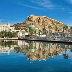 Widok na port i zamek Santa Barbara w Alicante. Luksusowe jachty odbijają się w spokojnej wodzie.