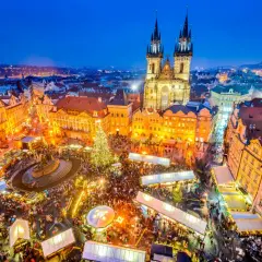 Tłoczny jarmark bożonarodzeniowy w Pradze, z oświetloną choinką i zabytkową architekturą w tle.