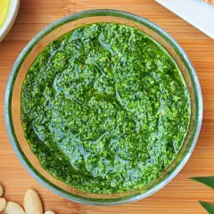 Aromatic pesto z czosnku niedźwiedziego w szklanej miseczce, otoczone migdałami i świeżymi liśćmi.