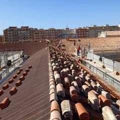 Trabajadores renuevan las cubiertas de tejas de un edificio, con pilas de tejas nuevas y viejas a la vista.
