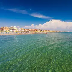 Słoneczny dzień nad morzem w Rzymie. Tłumy plażowiczów, kolorowe parasole i budynki wzdłuż wybrzeża.