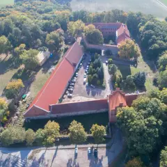 Zamek Bierzgłowski z lotu ptaka, otoczony jesiennym lasem. Widać czerwone dachy, dziedziniec z samochodami i otaczające tereny zielone.
