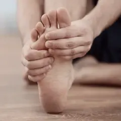 Uomo che si tiene il piede, mostrando i sintomi della metatarsalgia. Dolore sotto l'avampiede.