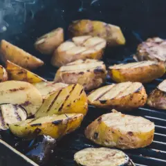 Pommes de terre coupées en quartiers, grillées à la perfection sur un barbecue, dégageant une fumée alléchante. Quelle pomme de terre barbecue !