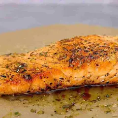 Succulento salmone in padella, dorato e profumato con erbe aromatiche, adagiato su carta da forno.