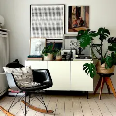 Gemütlich eingerichtetes schmales Reihenhaus: Schwarzer Schaukelstuhl mit Kissen, weißes Sideboard mit Pflanzen und Kunst.