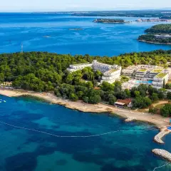Hotel Delfin Plava Laguna, otoczony zielenią, z basenami i plażą nad turkusowym morzem.