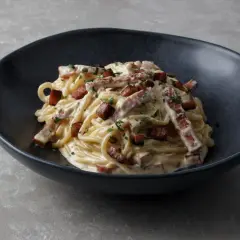Un plat de spaghetti crémeux, garni de morceaux de guanciale croustillant et de persil frais. La vraie recette carbonara italienne, un délice simple et authentique.