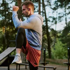 Mann im Freien beim **hit training**, hebt ein Knie, konzentriert sich auf seine Bewegung.