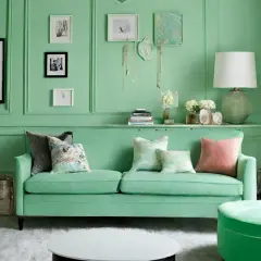 Ein Wohnzimmer in Mintgrün, das zeigt, wie man Mintgrün mischt. Ein grünes Sofa mit Kissen, ein runder Hocker und Kunst an der Wand.
