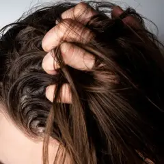 Mano revolviendo cabello oscuro y lacio. ¿Es mejor teñirse con el pelo sucio o limpio?