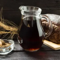 Dzbanek z ciemnym napojem, bochenek chleba, kłosy zboża i miseczka z mąką. Czy podpiwek ma alkohol? To pytanie nurtuje wielu.