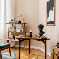 Kącik do czytania w stylu vintage: fioletowy fotel, drewniany stolik z biustem i książkami, regał pełen literatury.
