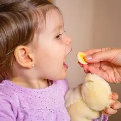 Małe dziecko z otwartymi ustami czeka na kawałek banana. Po biegunce u dziecka ważne jest nawadnianie i lekkie posiłki.