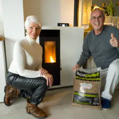 Pareja feliz junto a su nueva estufa de pellets, con una bolsa de combustible lista para la instalación.