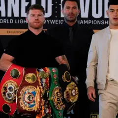 Canelo Alvarez, surrounded by championship belts, shows how good he is. He stands with Dmitry Bivol and Eddie Hearn.