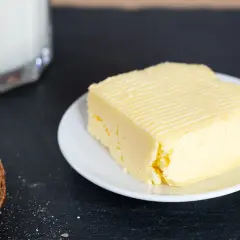 Frisch gemachte Butter auf einem Teller, daneben eine Scheibe Brot mit Butter bestrichen. So einfach kann Butter selber machen sein!