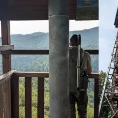 Widok z wieży widokowej na Bieszczady. Turysta z plecakiem i kijkami obserwuje krajobraz.