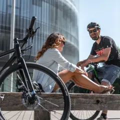 Ein Paar entspannt sich auf einer Holzbank mit Fahrrädern in einer modernen Stadt. Hier lebt es sich fahrradfreundlich.