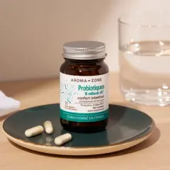 Bouteille de probiotiques Aroma-Zone sur une assiette avec des gélules, à côté d'un verre d'eau. Une cure probiotique pour le confort intestinal.
