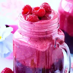 En härlig hallonsmoothie i ett glas med färska hallon på toppen. Ett perfekt smoothie recept för en solig dag.