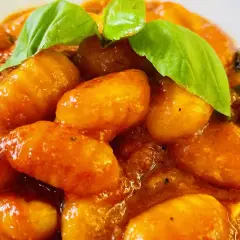 Gnocchi al pomodoro, soffici e avvolti in un sugo rosso brillante, guarniti con foglie di basilico fresco.