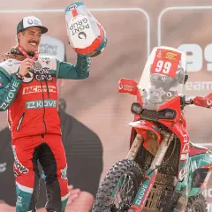 Piloto celebra victoria junto a su moto china Dakar. Casco y medalla en mano, luce orgulloso su equipación.