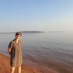 Mujer sonriente en la orilla de arena rojiza del lago Kariba, con el agua tranquila y el cielo despejado al fondo.