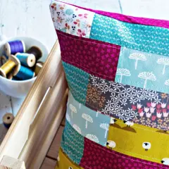 Buntes Patchwork-Kissen zeigt, wie man Stoffreste sinnvoll verwerten kann. Kleine Schafe und Blumenmuster zieren die Kissenhülle.