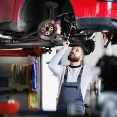 Mechanik w warsztacie sprawdza podwozie czerwonego samochodu na podnośniku.