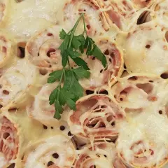 Pyszna tortilla z szynką i serem na ciepło, zapieczona do złotego koloru, udekorowana gałązką natki pietruszki.