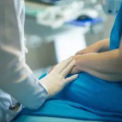 Lekarz w białej rękawiczce delikatnie dotyka dłoni pacjenta, oferując wsparcie w leczeniu wyrośli chrzęstno-kostnej.