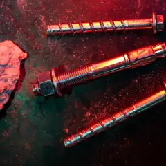 Tasselli e bulloni metallici, con un pezzo di cemento grezzo. La scena è illuminata da luci rosse e verdi, creando un'atmosfera drammatica, ideale per una tabella portata tasselli.