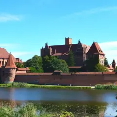 Potężny zamek Malbork z czerwonej cegły, otoczony murami obronnymi, góruje nad spokojną wodą.