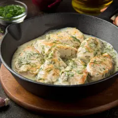 Pyszny kurczak w sosie śmietanowym, posypany świeżym koperkiem, podany w żeliwnej patelni.