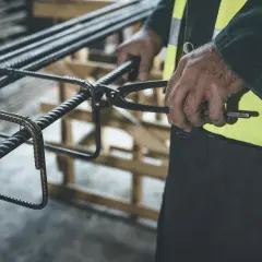 Budowlaniec zbroi beton, używając szczypiec. Dbałość o detale, jak inhibitor korozji, zapewnia trwałość konstrukcji.