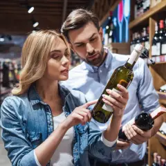 Para wybiera wino w sklepie. Kobieta wskazuje na etykietę, na której widnieje informacja, że produkt zawiera siarczyny.