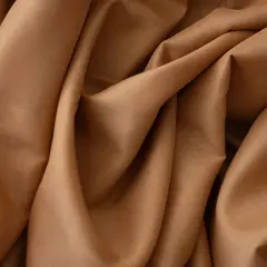 Gładki, brązowy krepa materiał układa się w miękkie fałdy, tworząc wrażenie luksusu i elegancji.